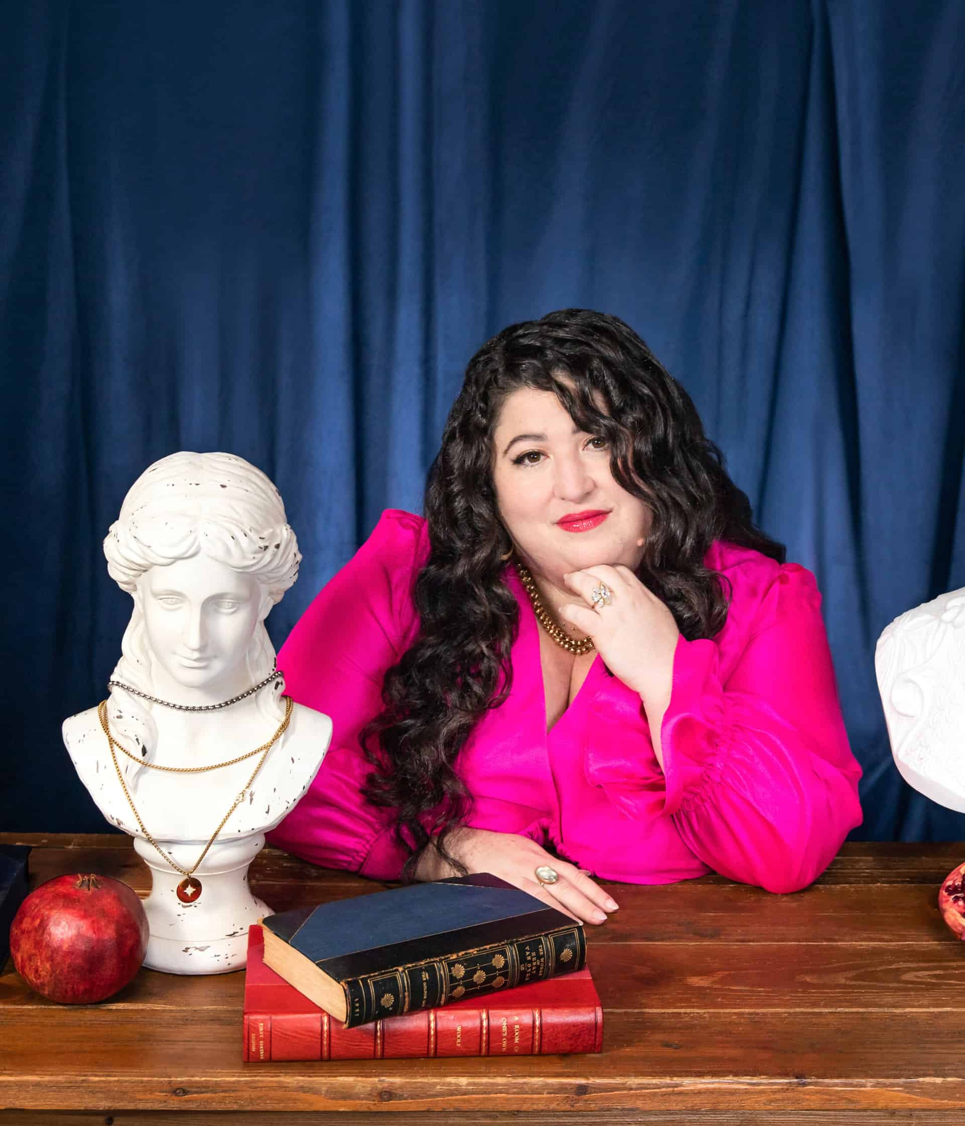 Kara Loewentheil sitting at a table with a sculpture bust, books and pomegranates.