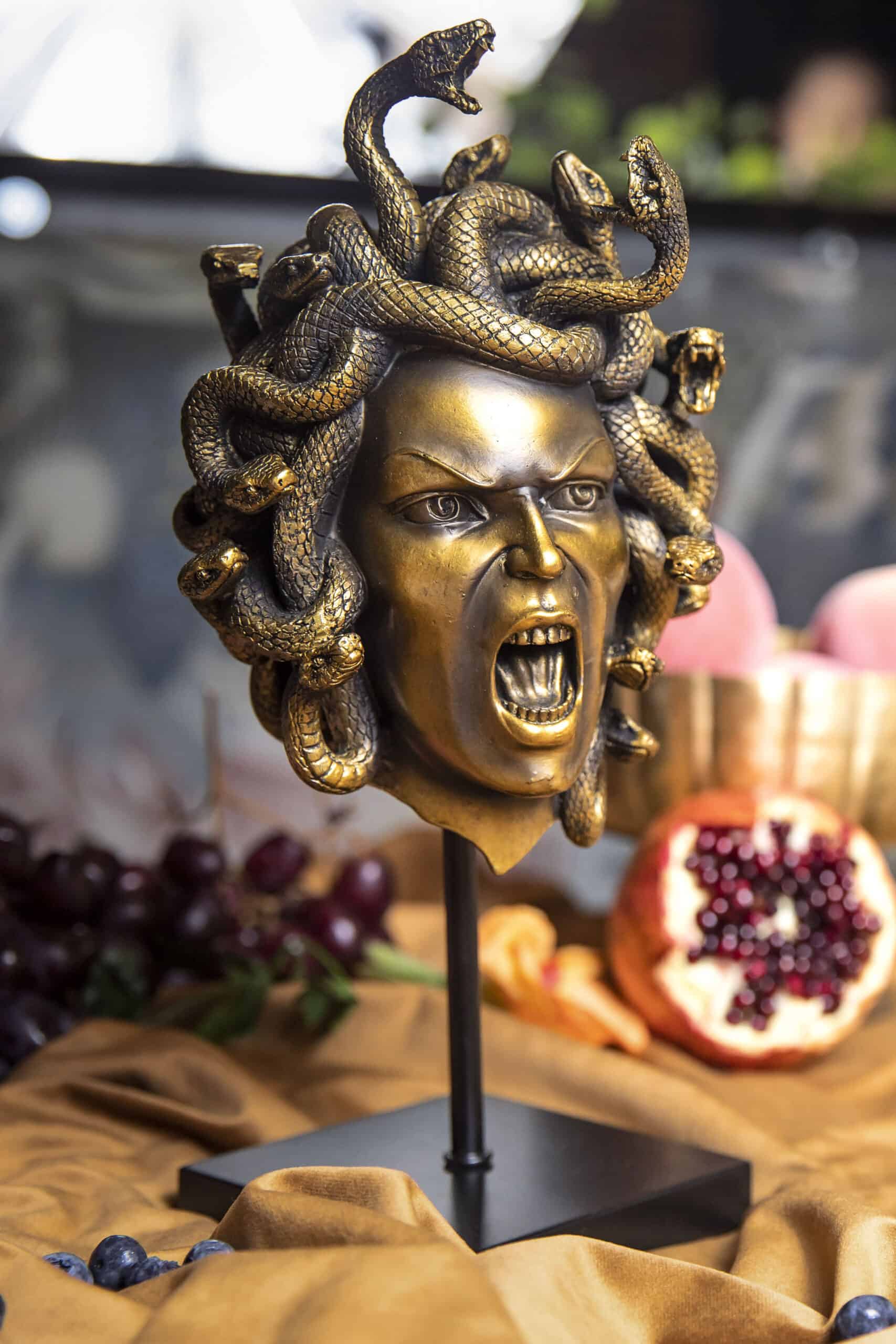 A gold statue of Medusa's head with various fruits in the background.